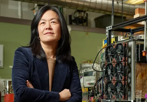 Professor Evelyn Wang ’00 sits beside a compact, portable water-harvesting device that she developed in collaboration with Professor Rohit Karnik of MIT and Krista Walton, then a professor at Georgia Tech. It’s designed for portable and emergency use. (Source: Ken Richardson, MIT Technology Review)